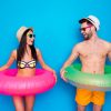 Happy rested young woman and attractive man with multi-colored lifebuoys at the waist laughing cheerfully and looking to each other an laughing isolated on blue background